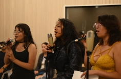 Tres mujeres jóvenes cantando frente a los micrófonos