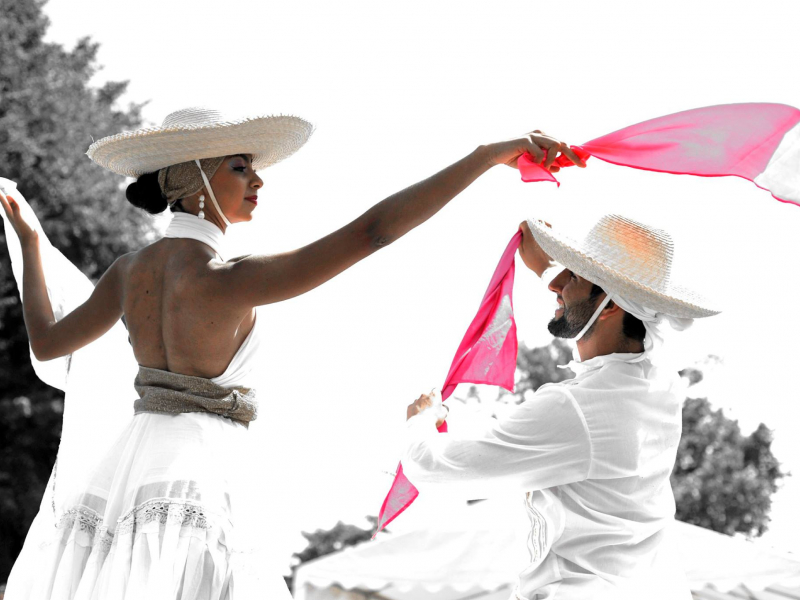 Hombre y mujer vestidos de blanco danzando con pañuelos rojos al aire libre.