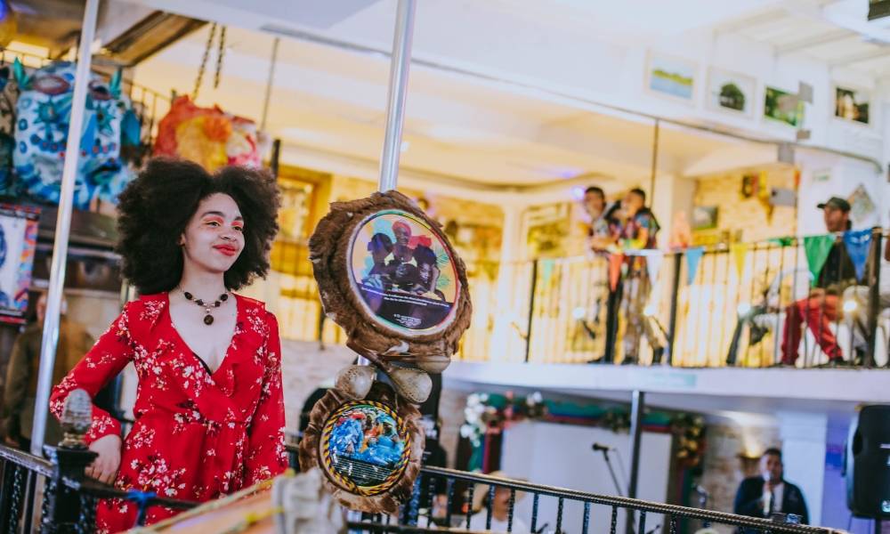 Artista en presentación escenica, joven con cabello afro y vestido rojo.