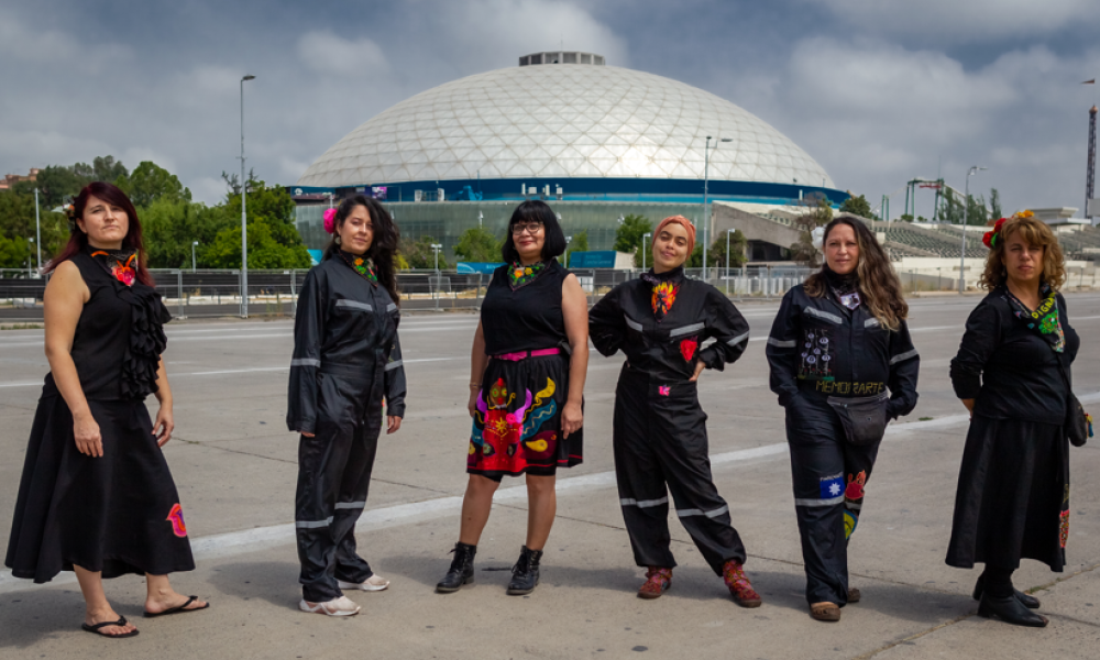 Seis mujeres vestidas de negro con bordados posando en exterior de día.