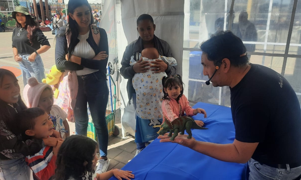 Hombre hablándole a niños con un dinosaurio de plástico en la mano