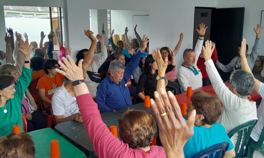 un grupo de adultos mayores están reunidos al rededor de una mesa