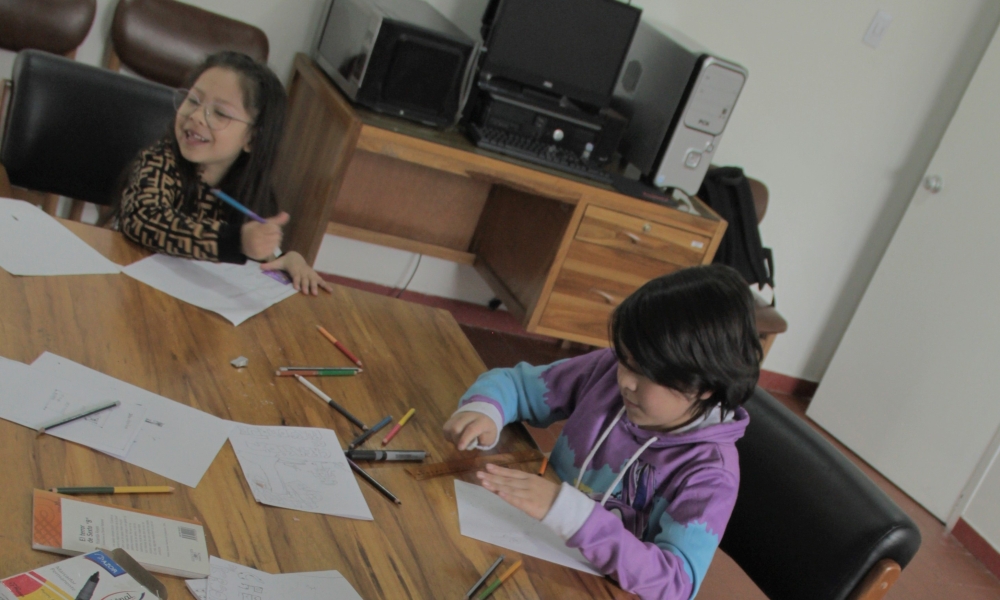 dos niños en una mesa usan colores para plasmar sus ideas en un papel