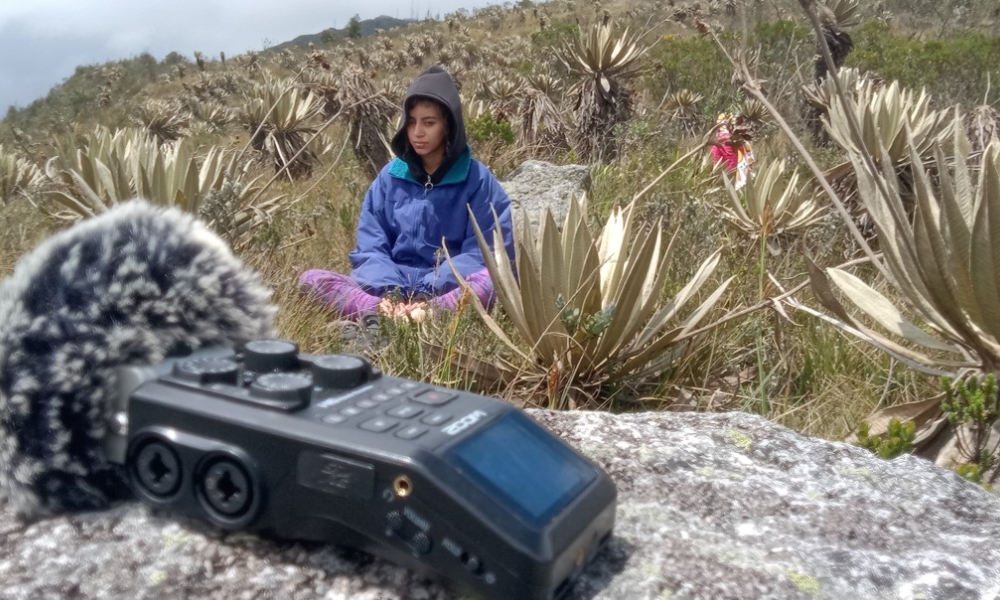 Imagen de mujer escuchando la naturaleza en montaña de Bogotá con un micrófono en frente.