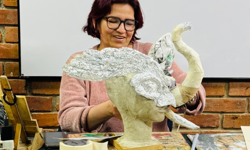 Una mujer sonrie frente a una figura que está haciendo en papel maché