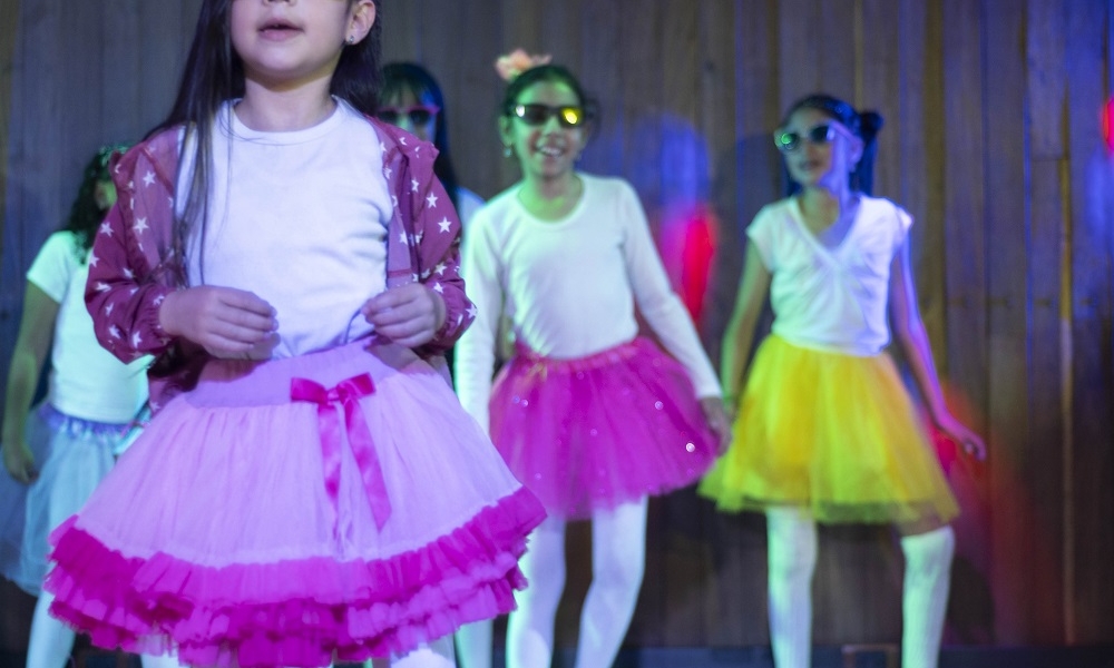 Una niña con gafas oscuras baila en un escenario. Fotografía por Lina Pachón.