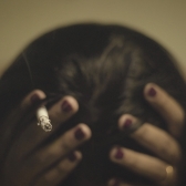 Mujer con cigarrillo en la mano tocándose la cabeza