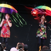 Artistas con sombrillas de colores en tarima cantando
