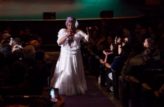 Mujer cantando en el escenario con vestido blanco.