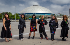 Seis mujeres vestidas de negro con bordados posando en exterior de día.
