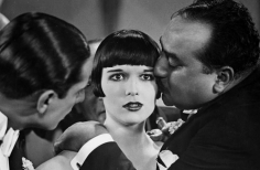 Foto en blanco y negro con dos hombre y una mujer, uno de ellos esta besando la mujer en la mejilla