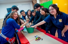un grupo de jóvenes introducen sus manos en un balde que contiene elementos de pintura