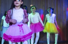 Una niña con gafas oscuras baila en un escenario. Fotografía por Lina Pachón.