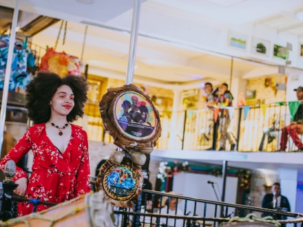 Artista en presentación escenica, joven con cabello afro y vestido rojo.