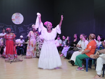 Una mujer vestida de blanco, alza sus brazos hacia el público