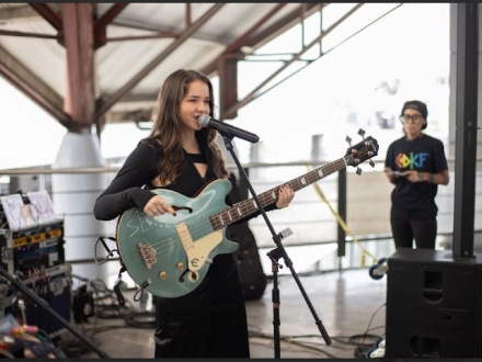 Emilia vestida de negro, con su guitarra y cantando en tarima 