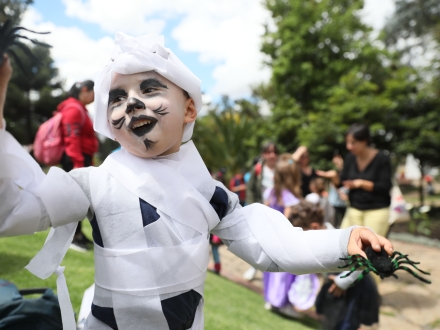 Niño disfrazado de momia con dos arañas en las manos juega en el parque de día.