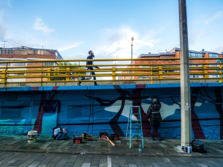 Artista urbano realiza su intervención en un puente de Bogotá mientras un hombre lo cruza