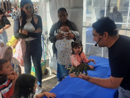 Hombre hablándole a niños con un dinosaurio de plástico en la mano