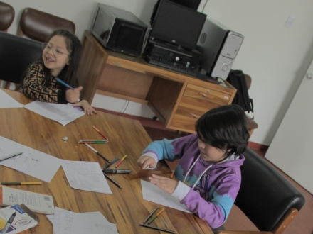 dos niños en una mesa usan colores para plasmar sus ideas en un papel