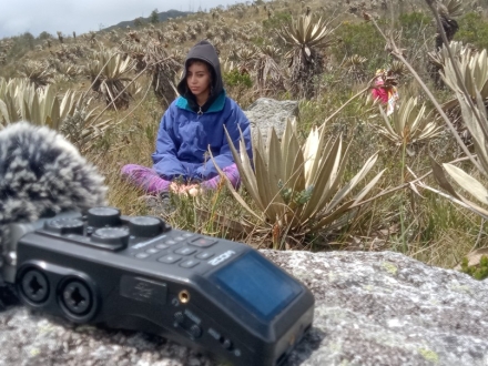 Imagen de mujer escuchando la naturaleza en montaña de Bogotá con un micrófono en frente.