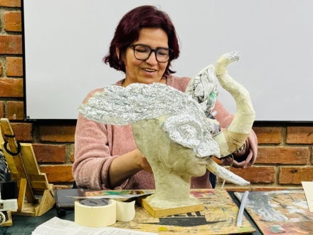 Una mujer sonrie frente a una figura que está haciendo en papel maché