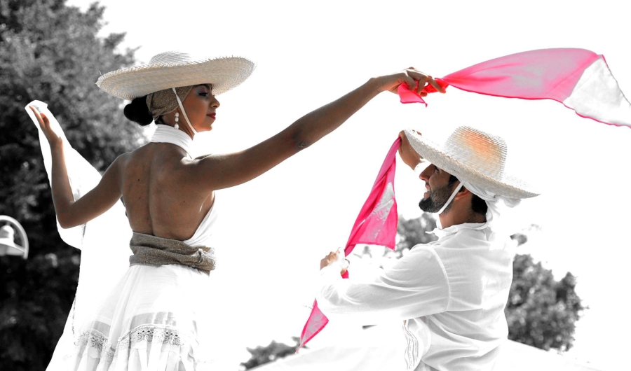 Hombre y mujer vestidos de blanco danzando con pañuelos rojos al aire libre.