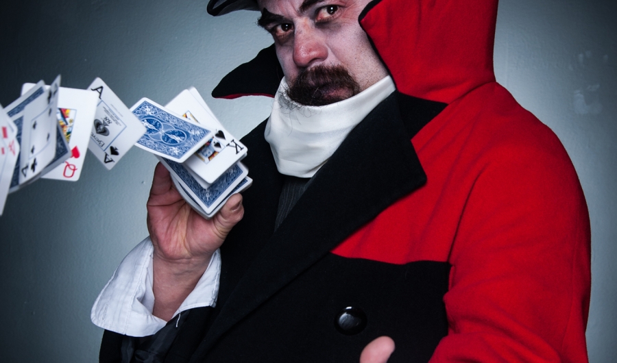 Hombre con capa roja y sombrero jugando con las cartas de un naipe.