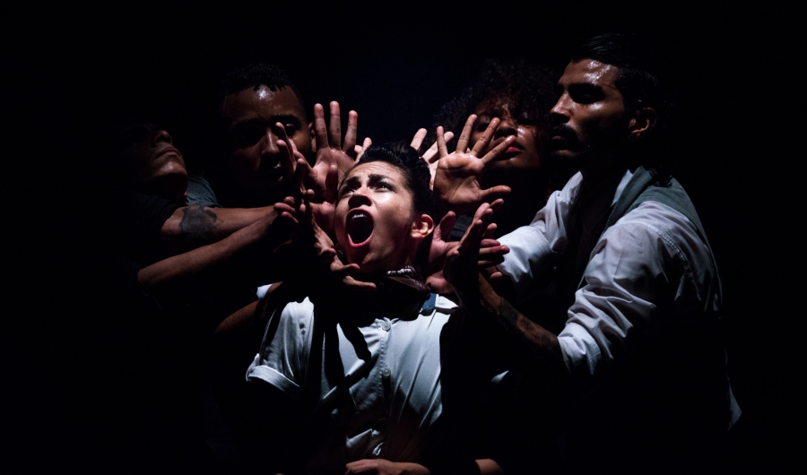 Varios hombres en el escenario, uno de ellos en actitud de grito rodeado por las manos de los otros.