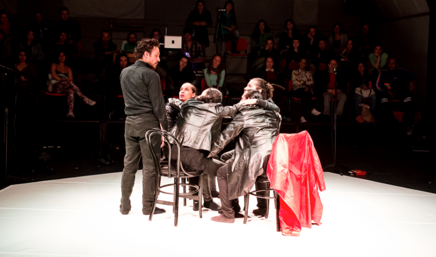 Cuatro actores que hacen parte de una escena de teatro con público al fondo