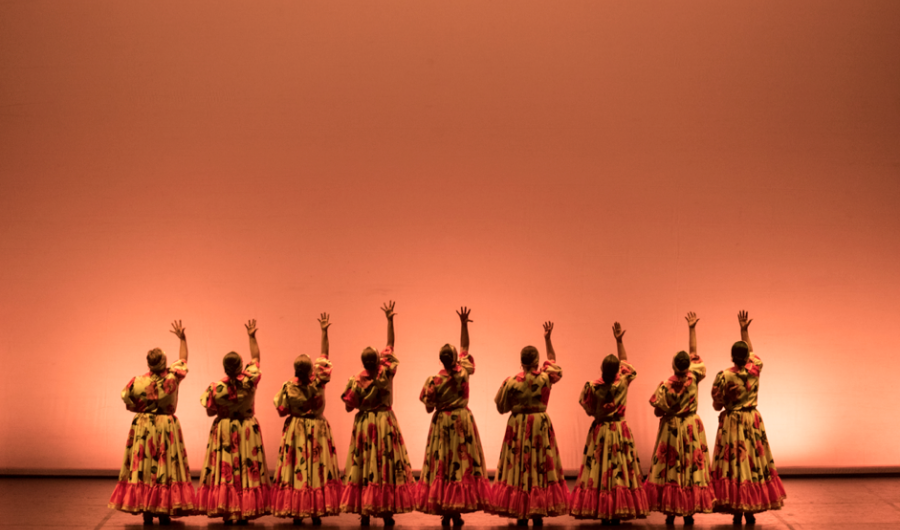 Mujeres  danzando en el escenario con trajes coloridos.