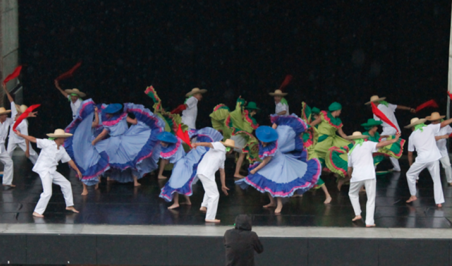 Personas danzando en el escenario con trajes coloridos.