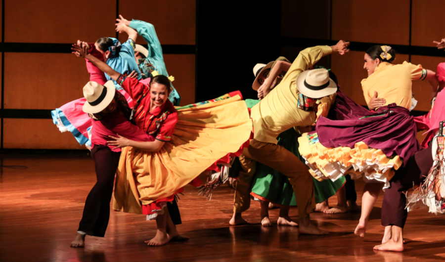 Personas de trajes coloridos y alegres bailando en un escenario