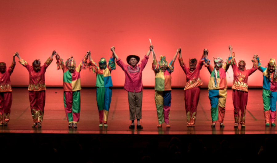 Personas en el escenario con trajes coloridos y brazos en alto