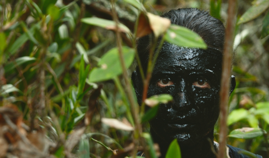 Rostro pintado totalmente de negro en medio de la vegetación