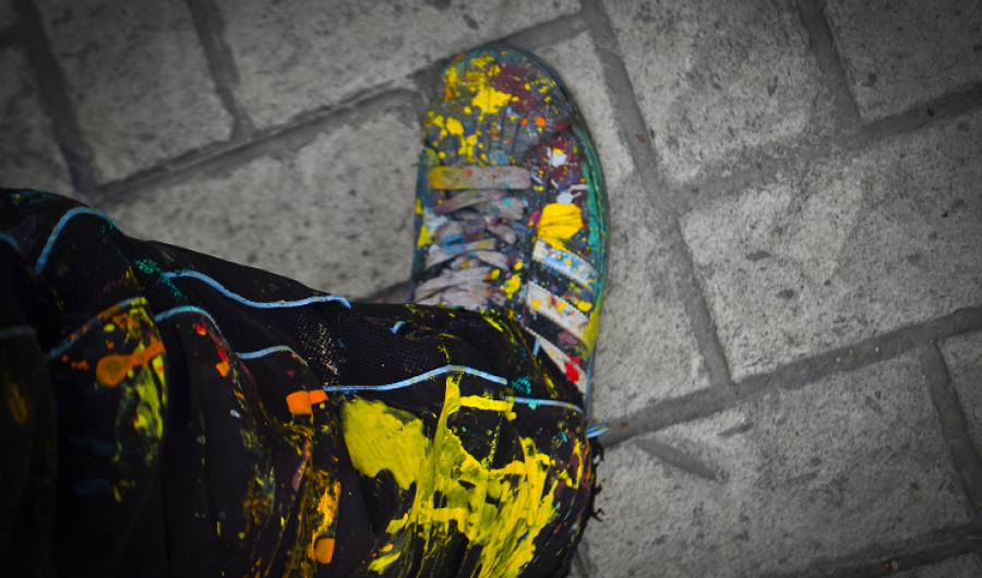 Zapato y pantalón de grafitero sobre baldosa pintados de muchos colores por pintura caída