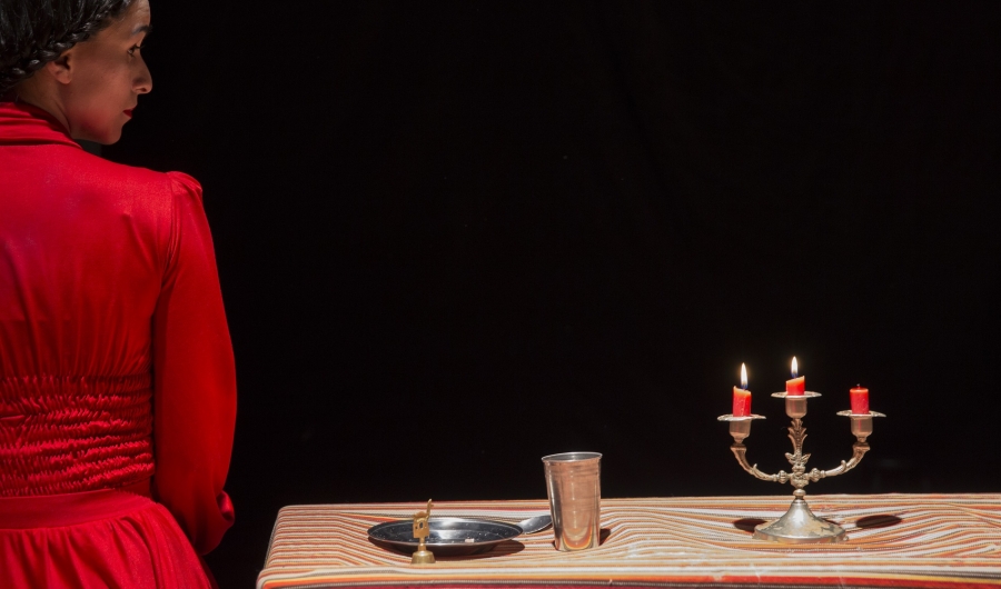 Mujer vestida de rojo al lado de una mesa con plato, vaso y velas.