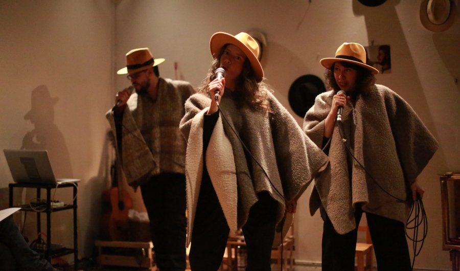 Dos mujeres y un hombre con sombreros y microfonos en escena