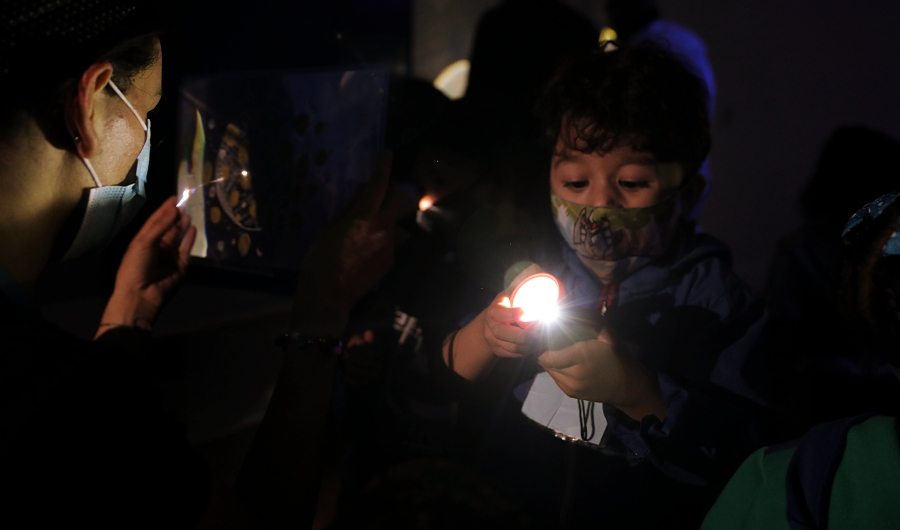 Niño jugando con una linterna y con una artista comunitaria