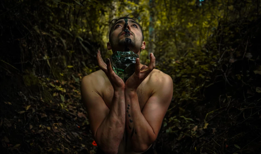 hombre sosteniendo una roca verde con sus manos con una selva de fondo. 