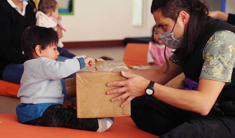 Niño jugando con una caja y un artista del Programa Nidos