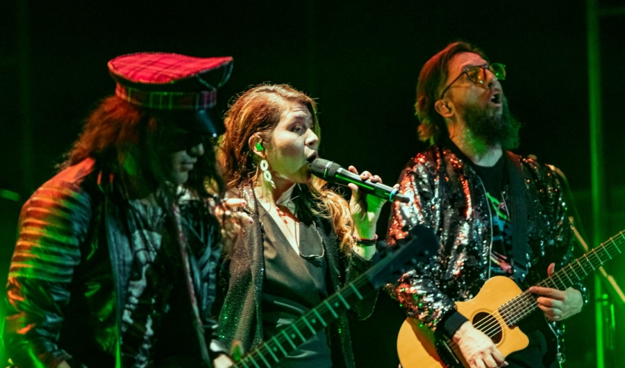 Una mujer cantando y dos hombres a su lado tocando guitarra