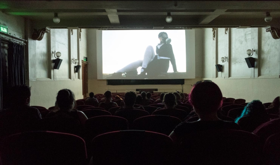 Personas en una sala de cine con una proyección de una mujer en blanco y negro. 