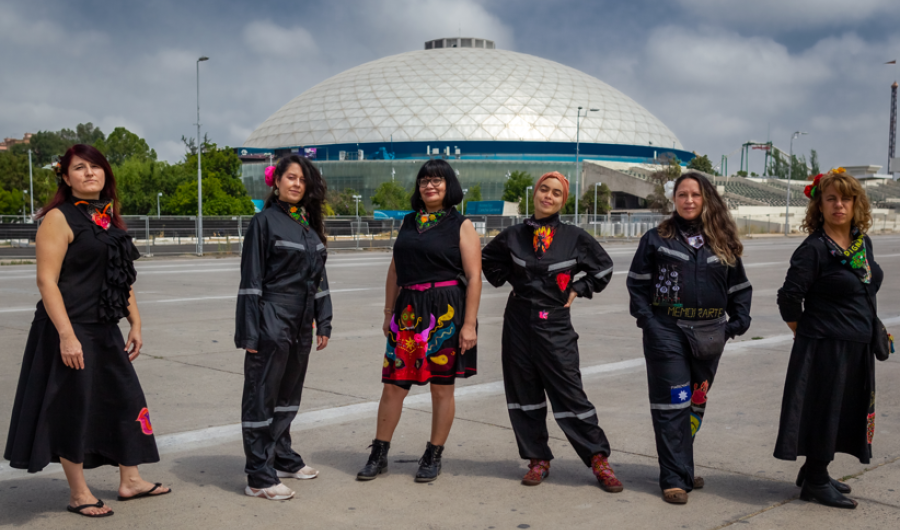 Seis mujeres vestidas con prendas negras y bordadas posando de pie de día.