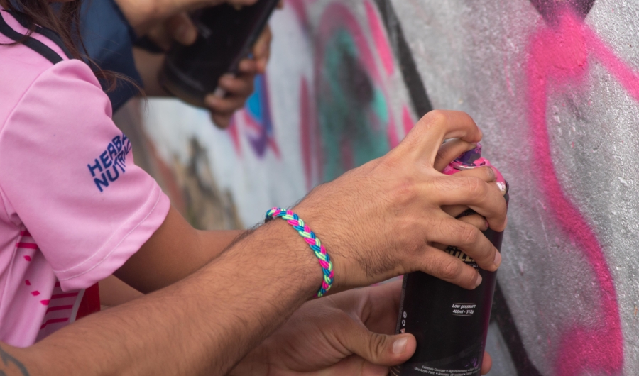 Plano cerrado de alguien utilizando una lata de pintura rosada en arte urbano para MAB