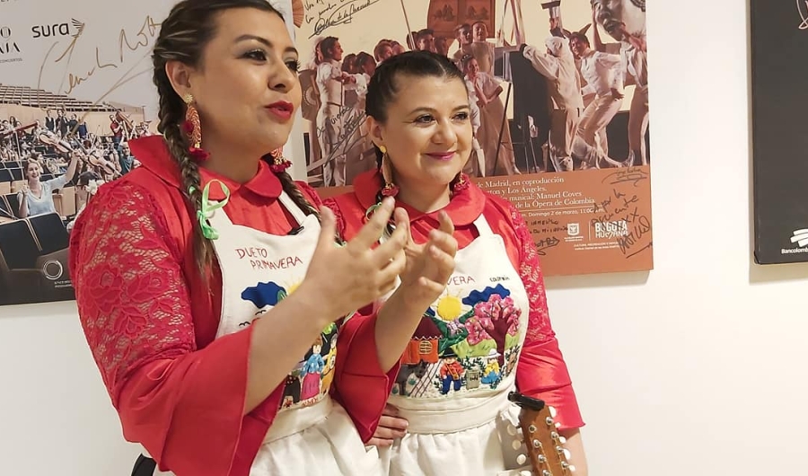 Dos mujeres peinadas con trenzas, vestidas con blusa roja y un delantal