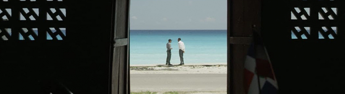 Fotografía de escena de Cocote con dos hombres en una playa vistos a través de una puerta
