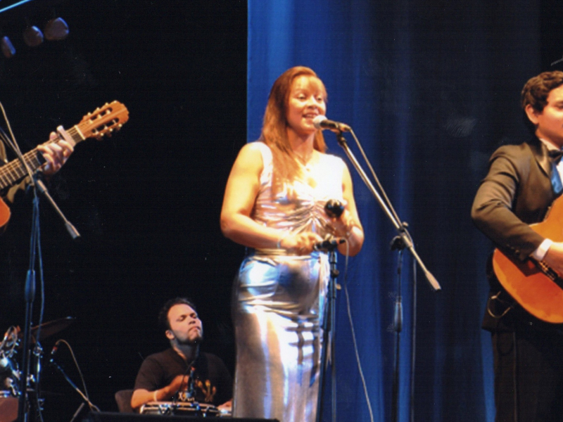 Dos hombres con guitarra y mujer cantando en el escenario