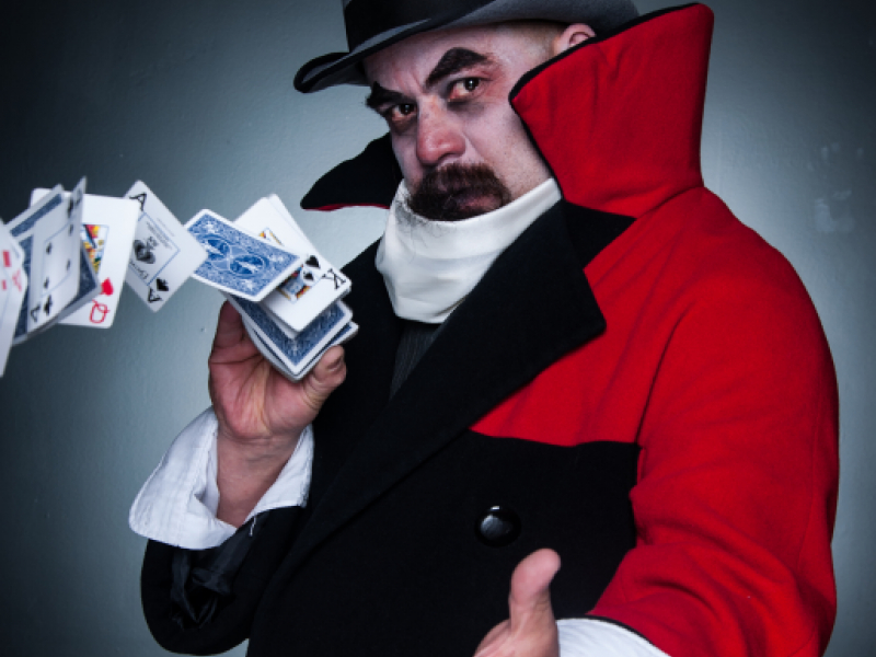 Hombre con capa roja y sombrero jugando con las cartas de un naipe.