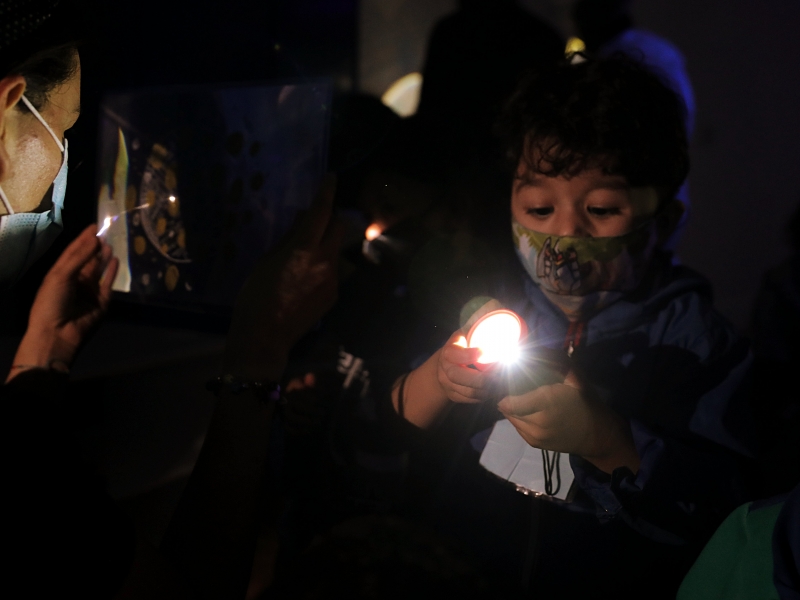 Niño jugando con una linterna y con una artista comunitaria